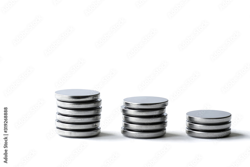 Three columns of different heights of round flat batteries on a white background. Macro mode. Copy space. Three columns of different heights of round flat batteries on a white background. Macro mode. Copy space.