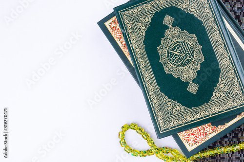 Holy Quran with arabic calligraphy meaning of Al Quran and tasbih or rosary beads over white background, copy space.