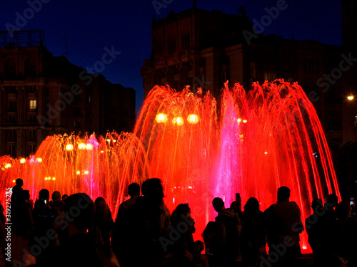 Red neon lights illuminate the jets of a powerful urban singing fountain in the late evening. photo