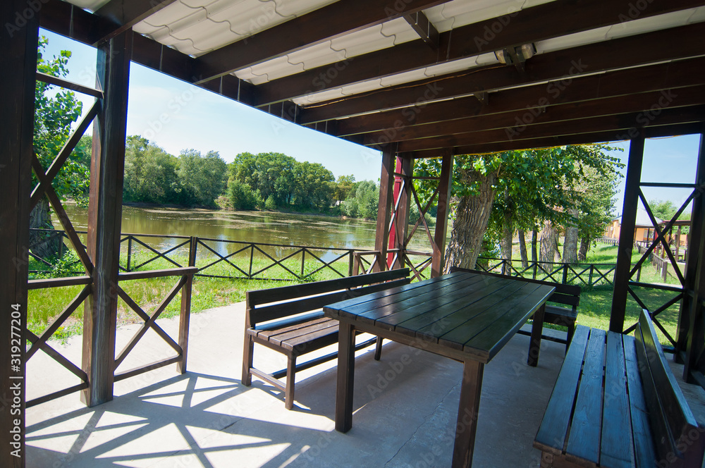 a spacious wooden gazebo with benches and a table near the lake overlooking the dense oak forest