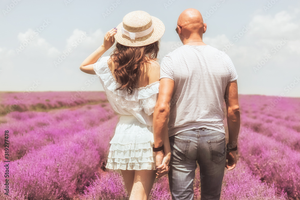 Back view lovely young couple at the lavender field, holding hands. Photo of beautiful young couple man and woman laughing and walking outdoor in lavender field