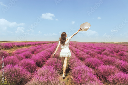 Fototapeta Naklejka Na Ścianę i Meble -  Woman on the lavender field. Woman in white dress and   hat  back view. Goes on lavender rows. girl in white dress and white hat is standing in the lavender field. Soft focus