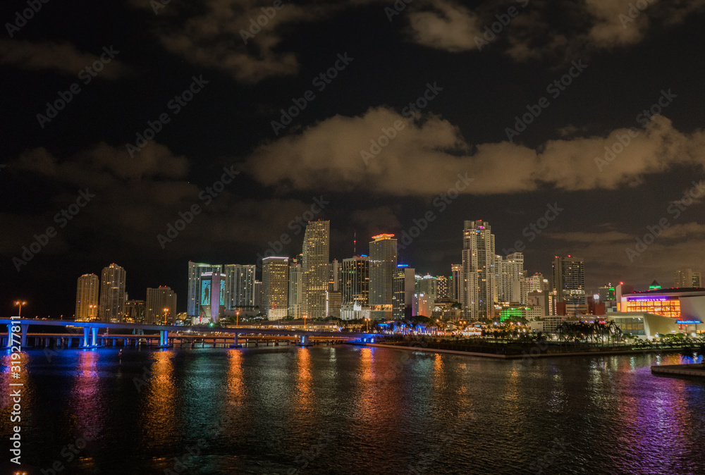 Miami city skyline panorama at dusk with urban skyscrapers and bridge over sea with reflection.