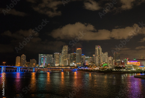 Miami city skyline panorama at dusk with urban skyscrapers and bridge over sea with reflection.