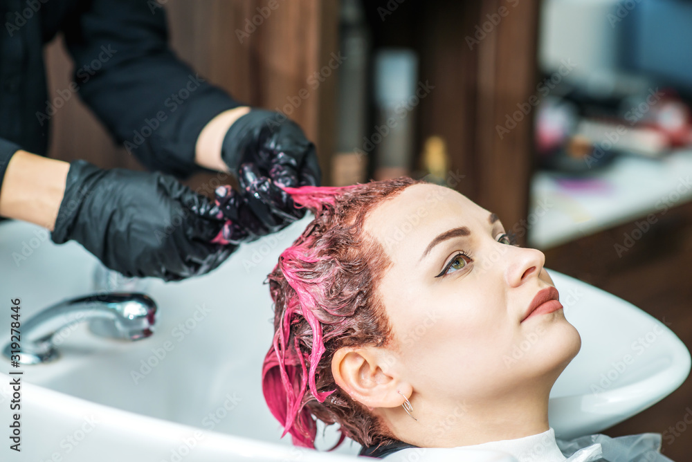 Hairdresser washing colored hair in pink of woman in sink, close up.