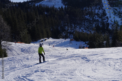 a man with a helmet in warm bright clothes goes snowboarding against the background of the mountain peaks of the sky and clouds. Active winter sport vacation or recreation.