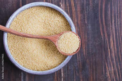 Dry couscous in a bowl and spoon on wooden background, photo