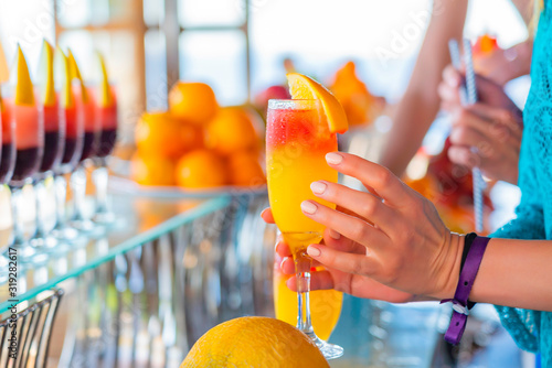 Girl take a glass with natural juice from the bar near the pool. Summer luxury tropical restaurant. Elegant cocktails set with fruits.