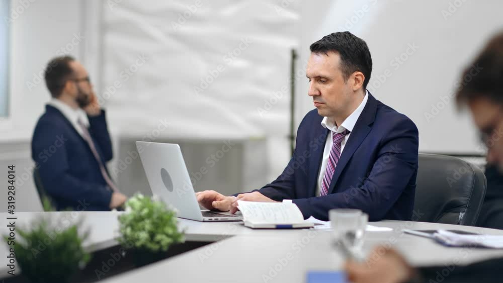 Focused businessman in suit enjoying job sitting on desk at white room interior RED raven camera Focused businessman in suit enjoying job sitting on desk at white room interior RED raven camera