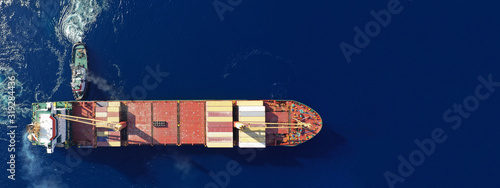 Aerial drone ultra wide top down photo of container ship cruising in Mediterranean port with deep blue sea assisted by tug boat photo