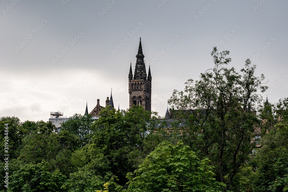 The ancient tower of the Gilbert Scott Building of University of Glasgow behind the green Kelvingrove Park in Scotland