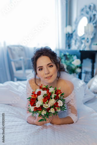 Beautiful happy bride on the bed with a wedding bouquet.