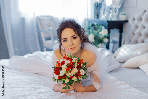 Beautiful happy bride on the bed with a wedding bouquet.