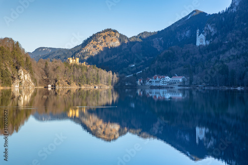 Stunning view of the Alpsee lake in winter on a sunny day with the Neuschwanstein Castle, Hohenschwangau Castle and Bavaria Alps in background, with beautiful reflections in water, Bavaria, Germany
