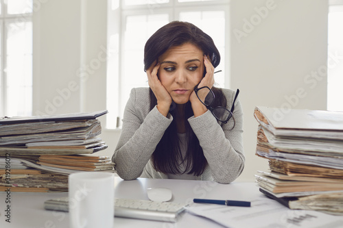 Woman brunette businesswoman in glasses with a mountain of documents on the table tired depressed emaciated disappointed depressive at the table in the office photo
