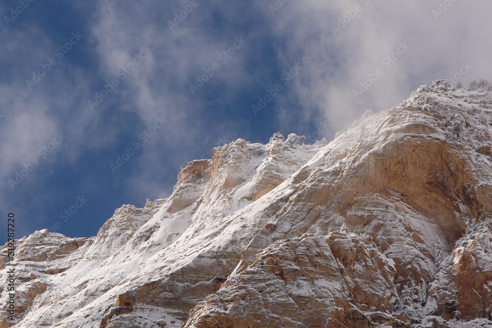 Clouds drift up against a deep blue sky from the face of the snow covered red rock mountains of Zion National Park after a winter storm in Southern Utah.