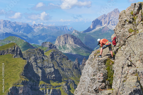 Man taking pictures secured to a via ferrata cable, high up on Delle Trincee klettersteig, in the Dolomites mountains, during a bright Summer day with scenic, panoramic views.