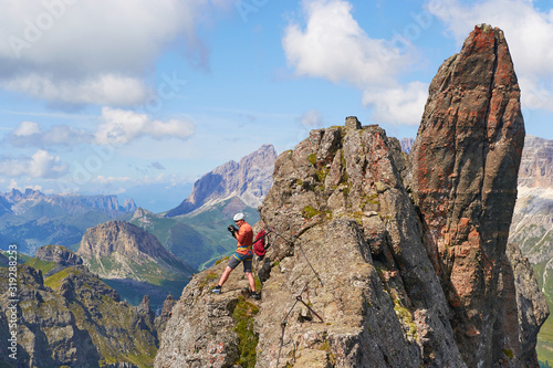 Adventure photographer looking around from a small ridge up on via ferrata Delle Trincee, in Dolomites mountains, Italy, on a sunny day. Pointy rock formations.