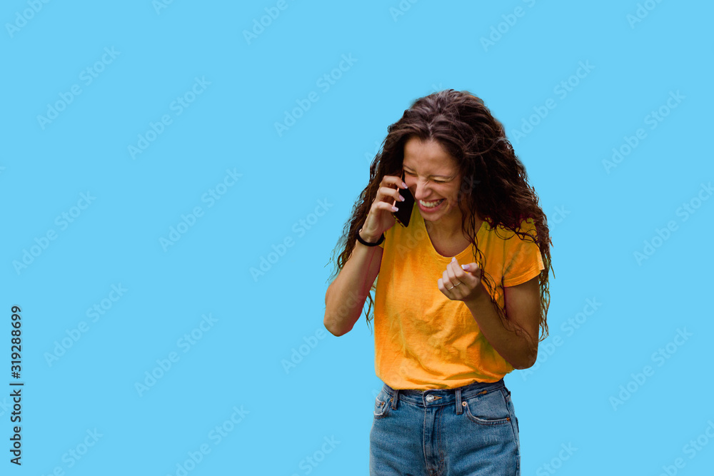 Brunette woman laughing while talking on the phone, on a colorful blue background Brunette woman laughing while talking on the phone, on a colorful blue background