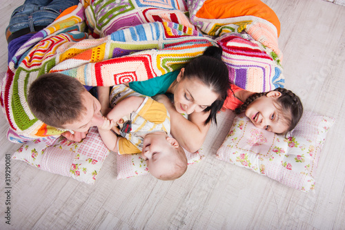 Obraz na płótnie Happy family lie on the floor under colorfull blanket and laught. Indoor photo shot w salonie