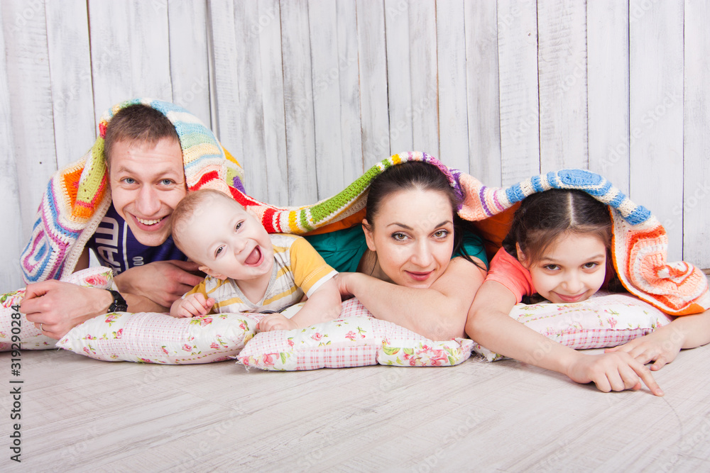 Happy family lie on the floor under colorfull blanket and laught. Indoor photo shot. Empty space for your text