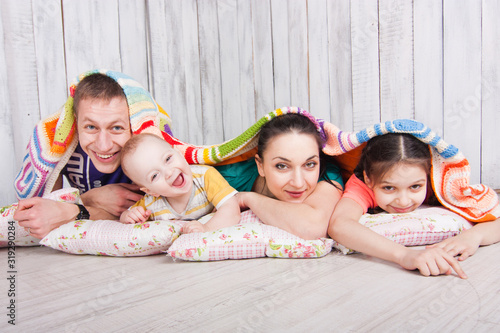 Obraz na płótnie Happy family lie on the floor under colorfull blanket and laught. Indoor photo shot. Empty space for your text w salonie