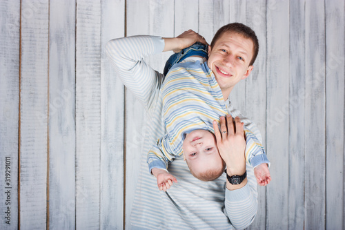Father plays with his little son. Boy hungs upside down. Indoor photo shot. Empty space for your text photo
