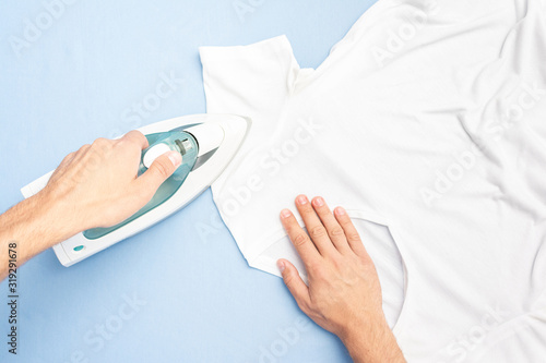 Concept of chores. Man ironing t-shirt, husband happy to do housework, top view, toned