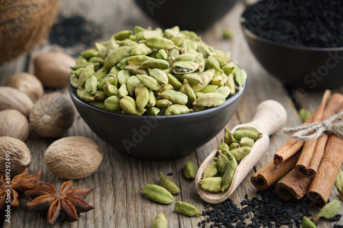 Green cardamom pods in black ceramic bowl. Aromatic spices: anise, gloves, black cumin seeds, nutmegs, cinnamon sticks, turmeric. Ingredients for healthy cooking. Ayurvedic treatments.