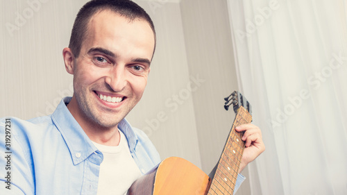Young guy smiles, man playing guitar at home, toned, portrait, 16:9