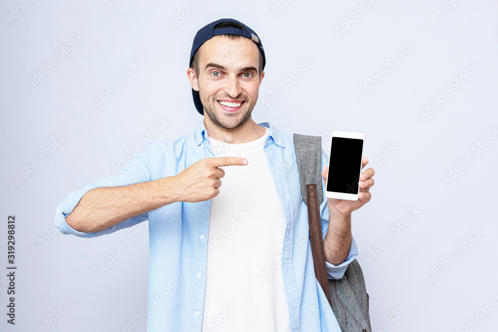 Young student with a backpack points to the screen of his phone. Portrait, gray background, copy space Young student with a backpack points to the screen of his phone. Portrait, gray background, copy space