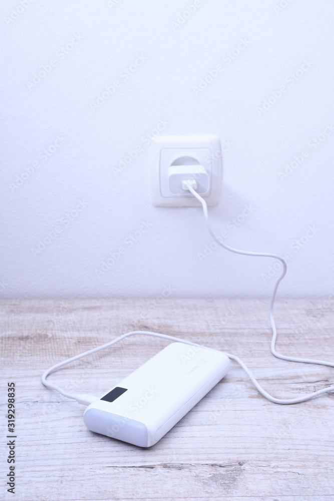 White phone power bank plugged in the socket on the wall for charging on wooden background White phone power bank plugged in the socket on the wall for charging on wooden background