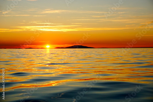 Orange and gold color tone beautiful sunset above the golden and blue sea surface on the island at the summer