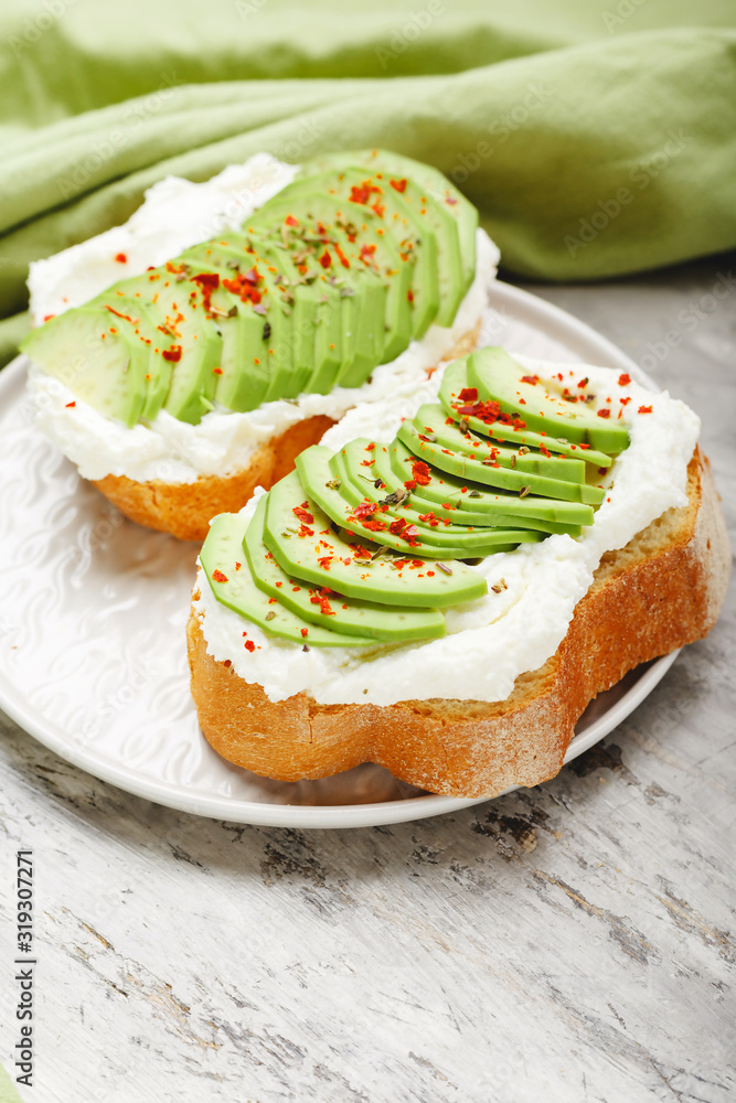 Two avocado toasts on gray plate, avocado sandwich. Fresh avocado sliced on toast of wheat bread, cream cheese.Avocado sprinkled with chili spices on gray concrete background with copy space
