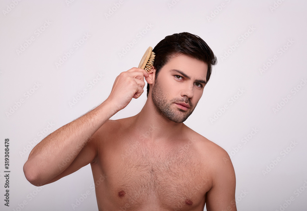 Charming sexy guy without a shirt combs his hair. Charming sexy guy without a shirt combs his hair.