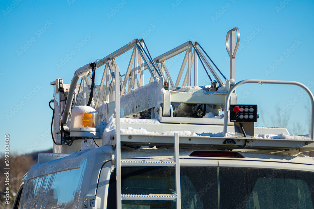 A close up and detailed view of the operating equipment atop a mobile works van, amber light and scissor lift on bucket truck. Under a blue winter sky