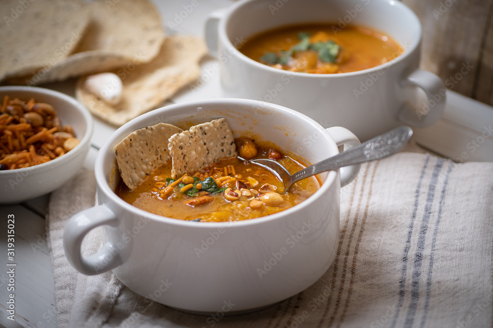 Vegan pumkin and spice soup garnished with peanuts and crackers on white wooden table Vegan pumkin and spice soup garnished with peanuts and crackers on white wooden table