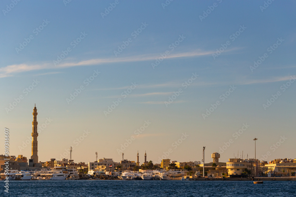 Hurghada, Egypt, a city at sunset. View of the ancient city from the red sea. Panoramic view. A port with ships and a residential area with a mosque.
