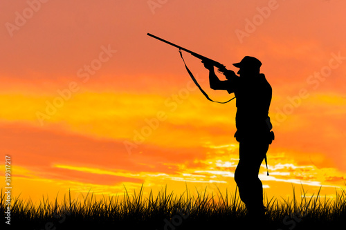 Silhouette of a hunter with a gun in the reeds against the sun, an ambush for ducks with dogs