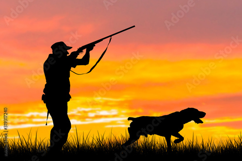 Silhouette of a hunter with a gun in the reeds against the sun, an ambush for ducks with dogs