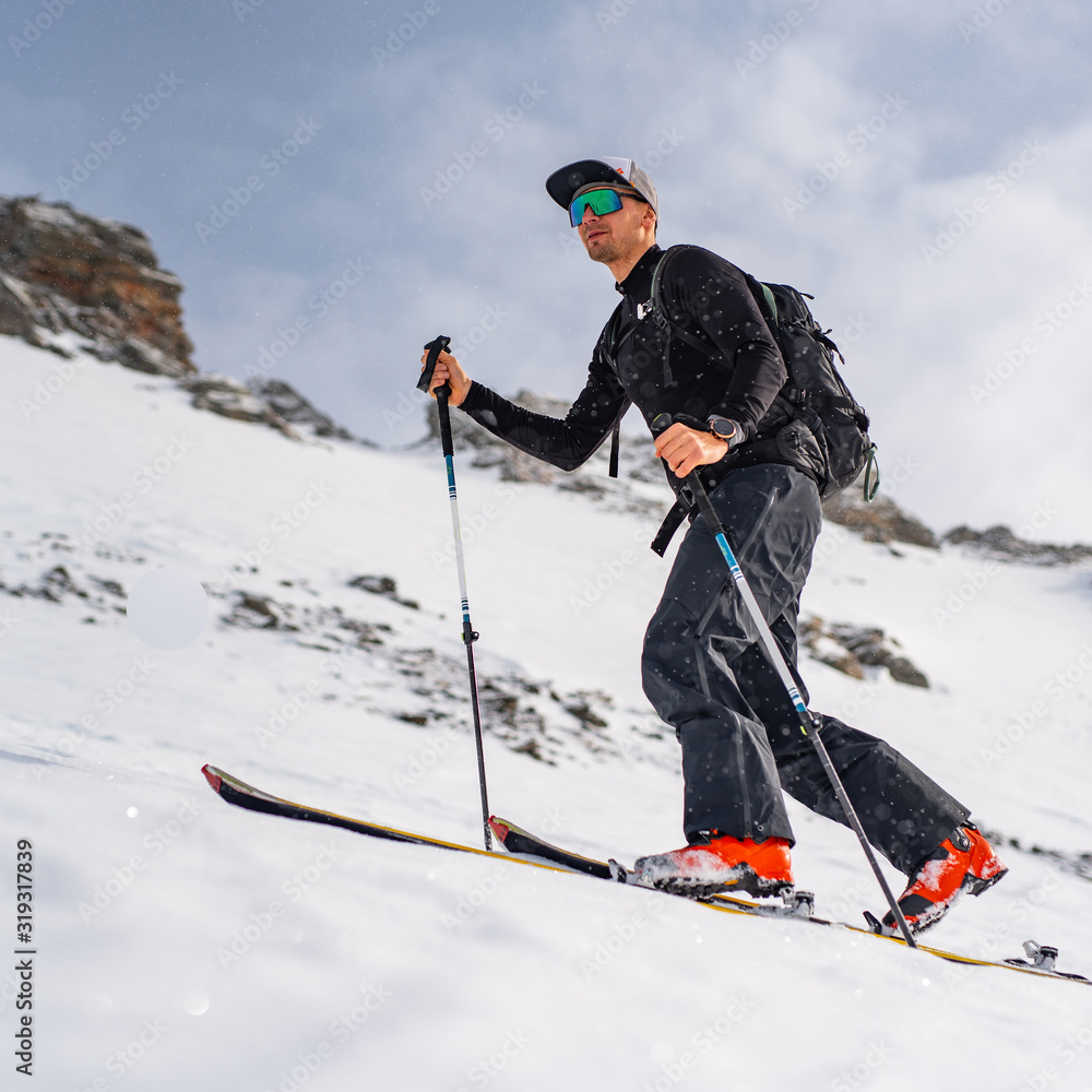 Ski touring man reaching the top in snow covered mountains, at sunny day. Snow and winter activities, skitouring in Alps