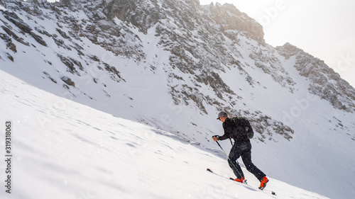 A skier in black jacket is climbing the hill using skitour equipment. Ski Touring in mountains.