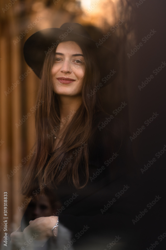 Outdoor photo of brunette lady posing on tree background in autumn day.Fashion street style portrait.Girl wearing dark casual clothes and dark hat .Fashion concept. Outdoor photo of brunette lady posing on tree background in autumn day.Fashion street style portrait.Girl wearing dark casual clothes and dark hat .Fashion concept.