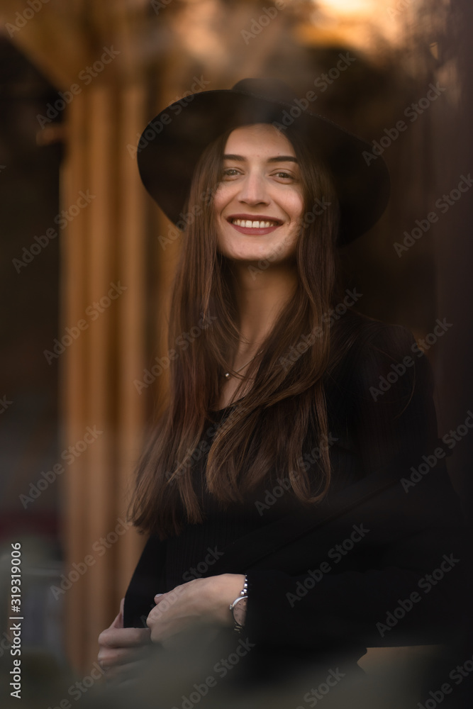 Outdoor photo of brunette lady posing on tree background in autumn day.Fashion street style portrait.Girl wearing dark casual clothes and dark hat .Fashion concept. Outdoor photo of brunette lady posing on tree background in autumn day.Fashion street style portrait.Girl wearing dark casual clothes and dark hat .Fashion concept.