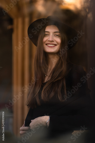 Outdoor photo of brunette lady posing on tree background in autumn day.Fashion street style portrait.Girl wearing dark casual clothes and dark hat .Fashion concept.