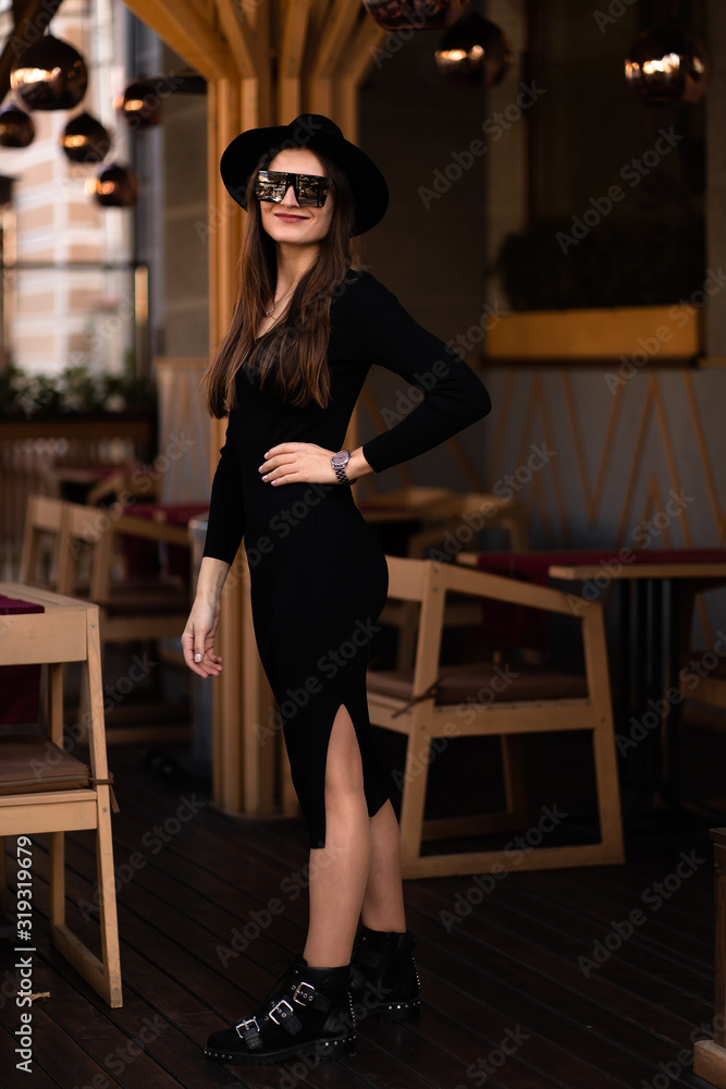 Photo of brunette lady posing on wooden background in cafe.Fashion style portrait. Girl wearing dark casual dress, sunglasses and dark hat .Fashion concept. Photo of brunette lady posing on wooden background in cafe.Fashion style portrait. Girl wearing dark casual dress, sunglasses and dark hat .Fashion concept.