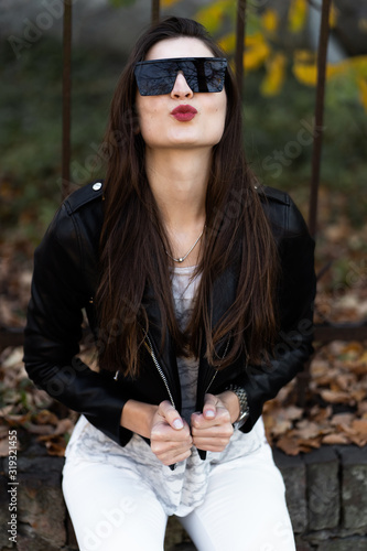 Obraz na płótnie Outdoor fashion portrait of stylish young woman having fun, emotional face , laughing, Urban city street style.Girl wearing white pants,t-shirt, black leather jacket , sunglasses and dark hat Fashion. w salonie