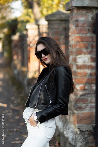 Obraz na płótnie Outdoor fashion portrait of stylish young woman having fun, emotional face , laughing, Urban city street style.Girl wearing white pants,t-shirt, black leather jacket , sunglasses and dark hat Fashion. w salonie
