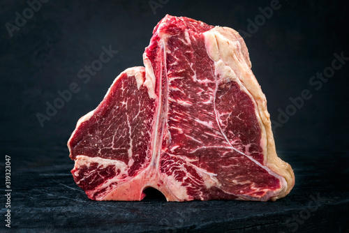 Raw dry aged wagyu porterhouse beef steak with large fillet piece as closeup on a black burnt wooden board with copy space