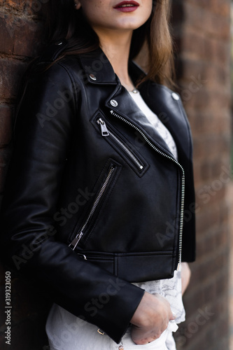 Hipster outfit. Model posing in street, wearingwearing white pants,t-shirt, black leather jacket and dark boots . Female fashion concept.